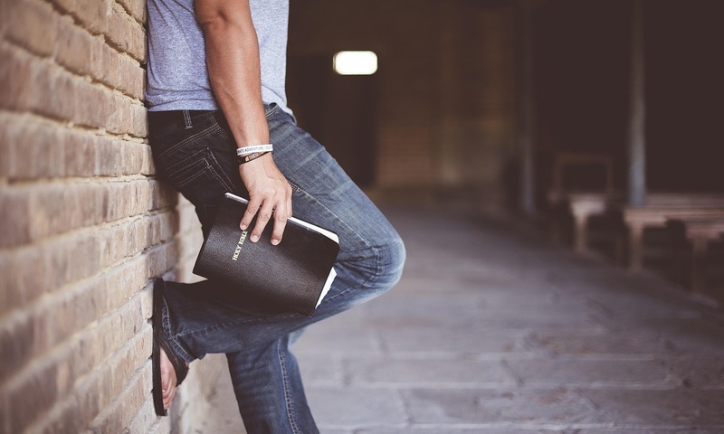image shows a man leaning against a wall with a Bible 