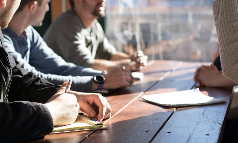 Image shows a group of people sitting at a table with journals open