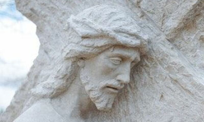 Stone statue of Jesus looking distressed with the cross