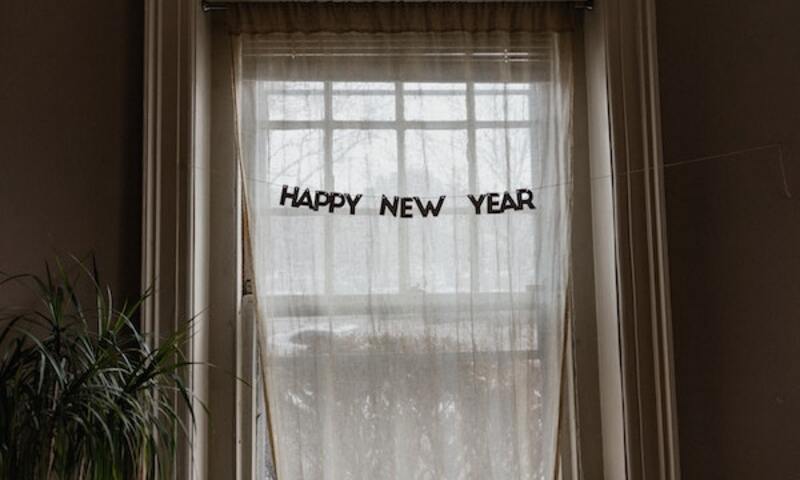 Image shows a "Happy New Year" sign hanging in a window. 