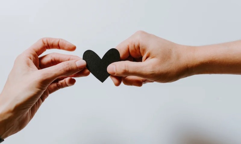 Image shows one hand passing a heart to another hand. 