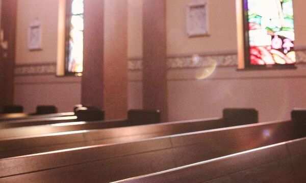 Image shows pews in a church with light coming through stained glass window