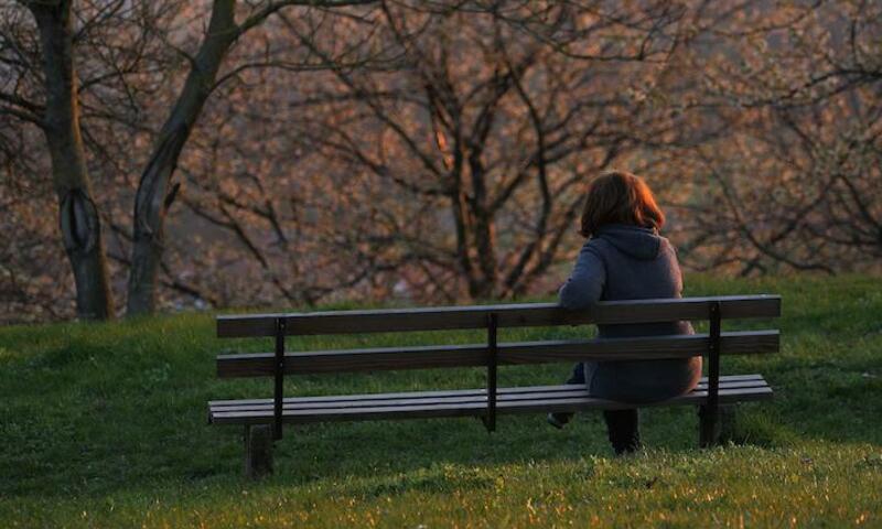 Image shows the back of a woman on a bench surrounded by trees 