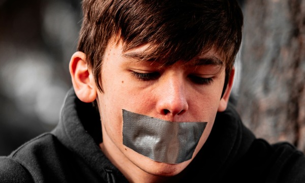 image shows a boy with tape over his mouth