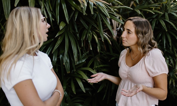 Woman shrugging shoulders and looking confused at other woman she is speaking with