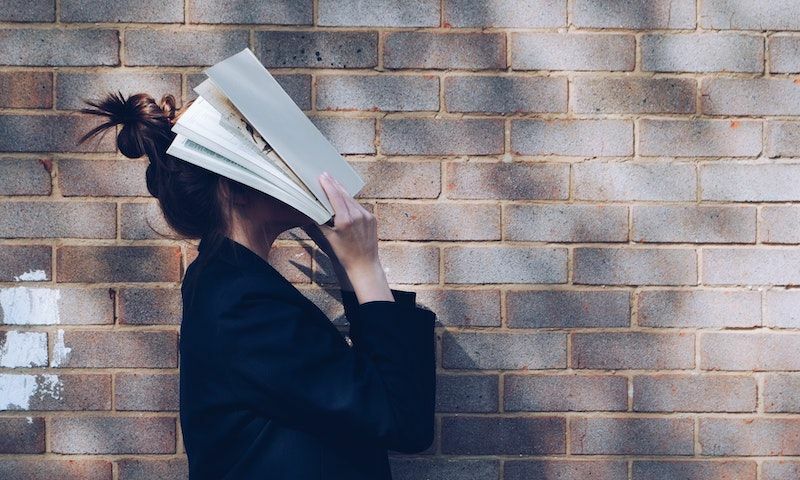 Student holding book over her face, overwhelmed