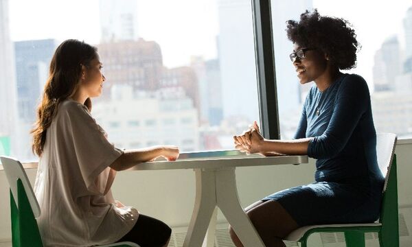 Image shows two women sitting at a table and having a deep conversation