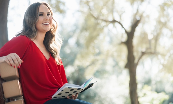 Young lady in a red sweater holds a journal in her left hand while sitting on park bench 