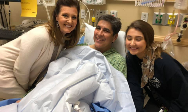 Chris Grace smiles from a hospital bed alongside his wife, Alisa, and their daughter during cancer treatment and recovery.