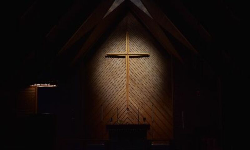 Image shows cross in church sanctuary with lights shining on it. 