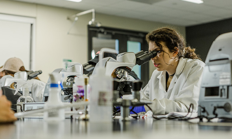 Woman looks through microscope in science lab at Biola University