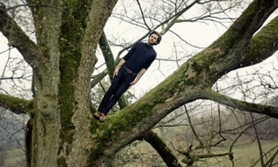 photograph of a man tilting sideways standing on a tree