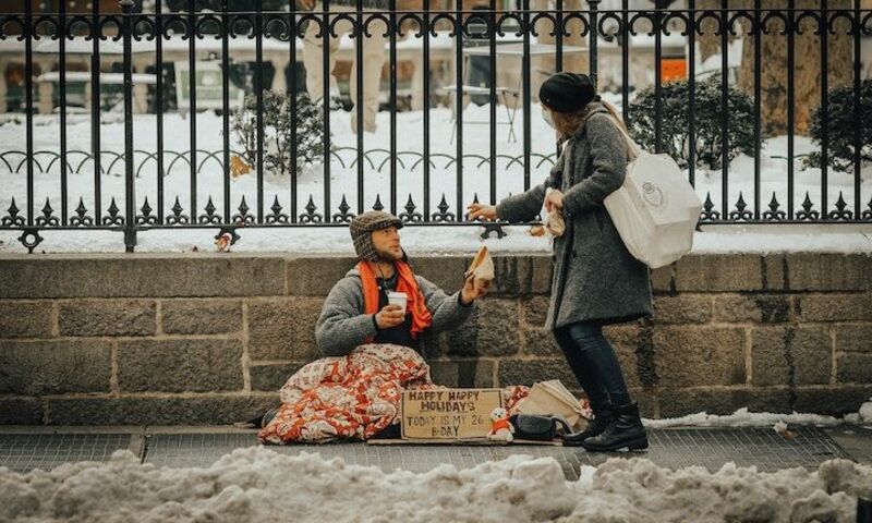 Image shows a woman handing something to a man sitting on the ground. 