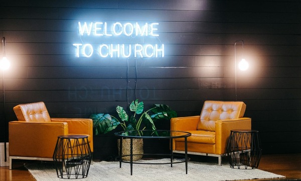 image shows two chairs and a welcome to church sign in neon