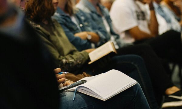 Congregation sitting in church with journals and Bibles on laps. 