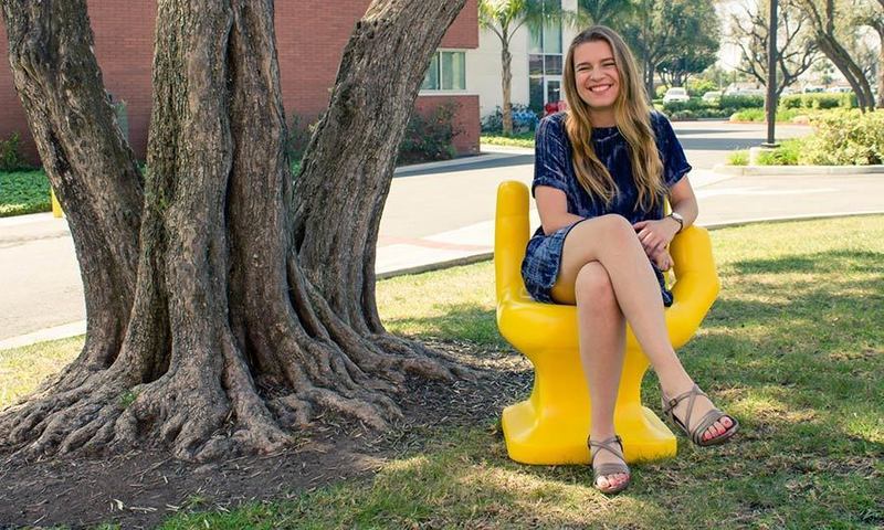 Female student sitting on yellow hand sculpture