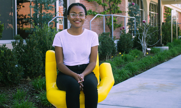 Female student sitting in yellow hand sculpture