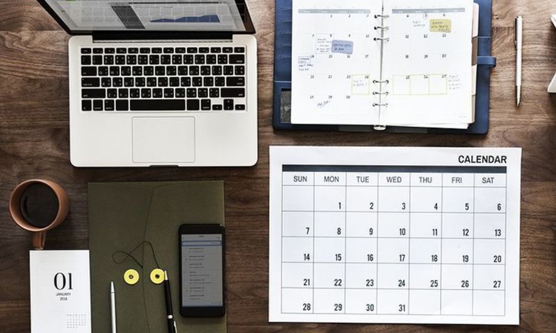 laptop, calendar, phone, cup and pens on a wood desk