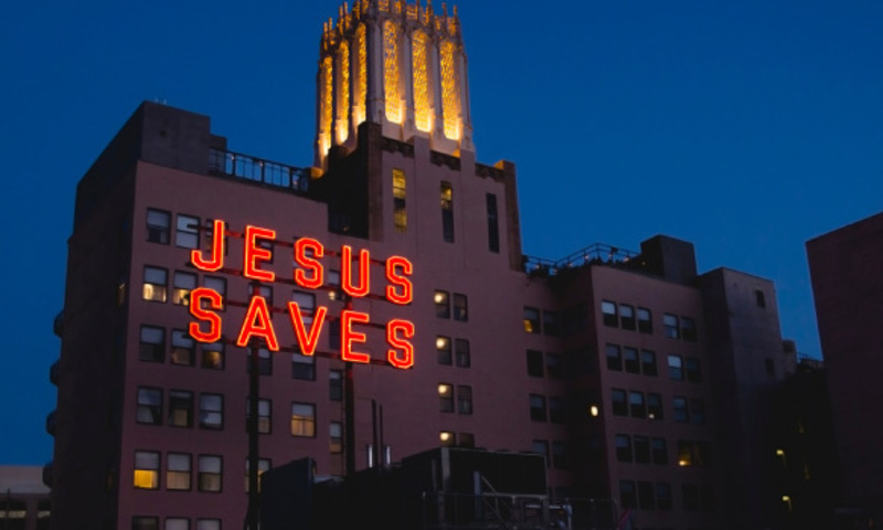 an illuminated sign reading 'Jesus Saves' on top of a large multi-story building