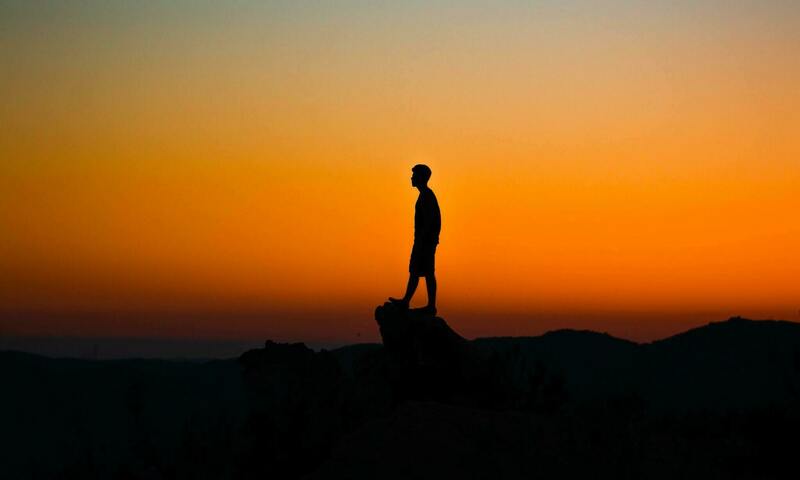 person on cliff at sunset