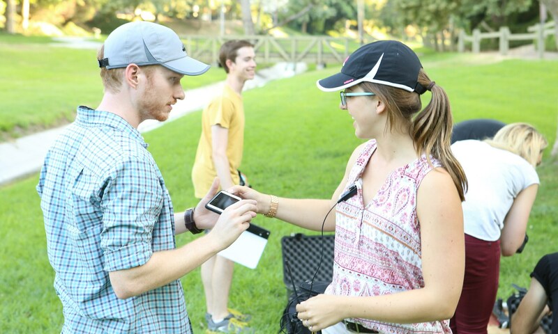 A young man talking to a young woman wearing a mic outdoors 