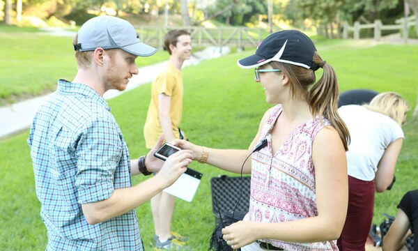 A young man talking to a young woman wearing a mic outdoors