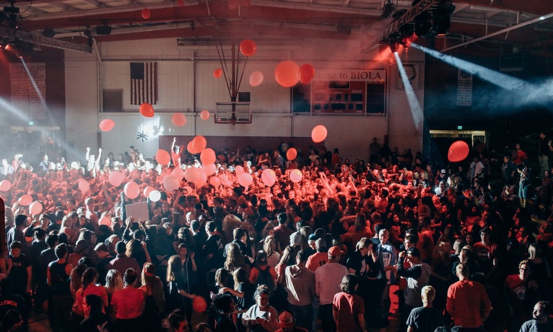 A crowd of people in the gym with balloons and spotlights