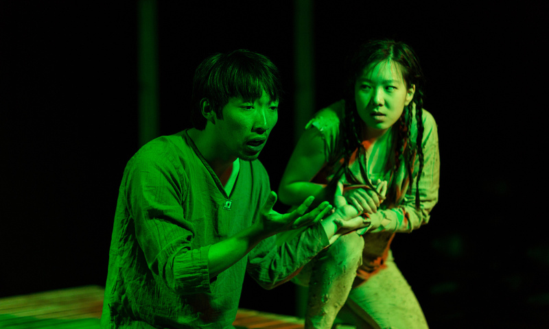 A young man and woman on stage with dramatic lighting