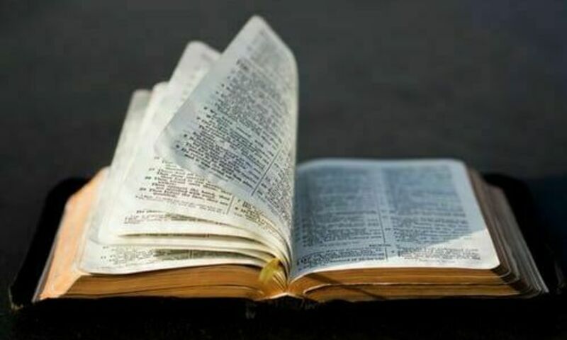 Open Bible on black surface with pages mid-turn