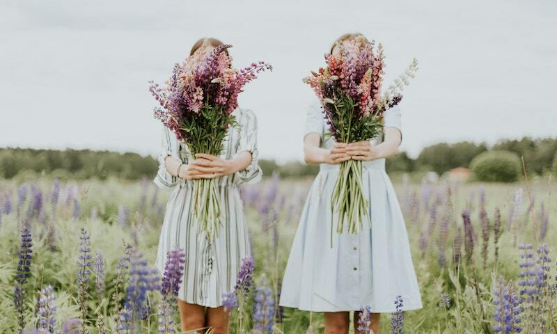 Two women standing with flowers in front of their faces. 