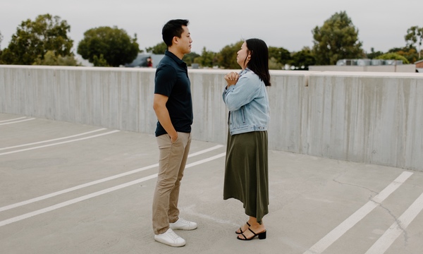 A couple stands facing each other in conversation on an outdoor parking structure.