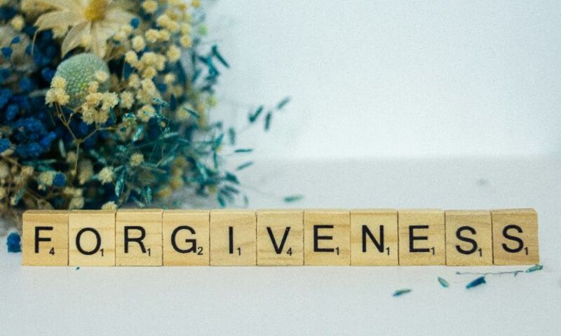 Image shows scrabble tiles spelling out forgiveness on a table with flowers in background