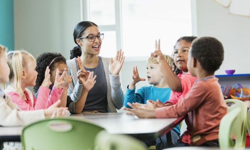 Image shows a teacher working with young students