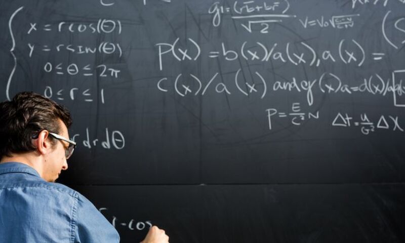 Image shows a math student working on problems on a blackboard