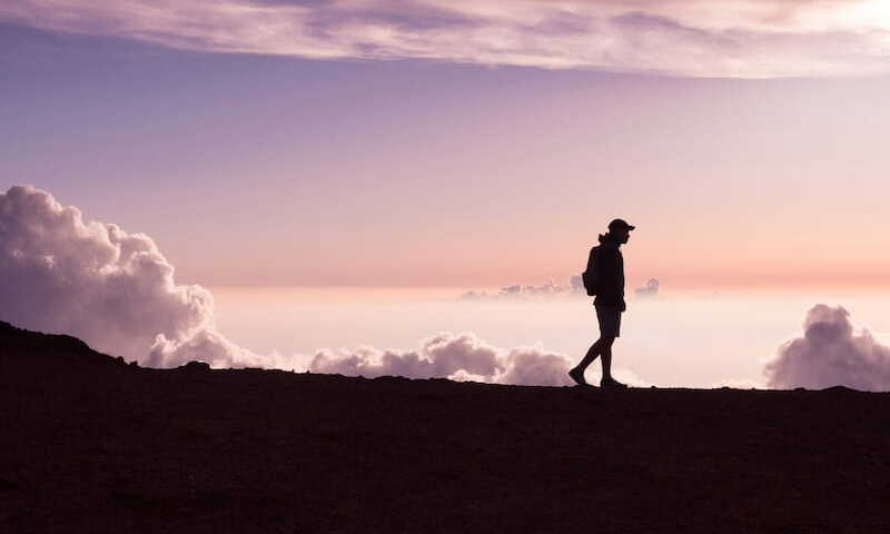 Silhouette of person walking under white clouds