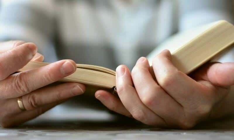 Image shows hands holding an open book 