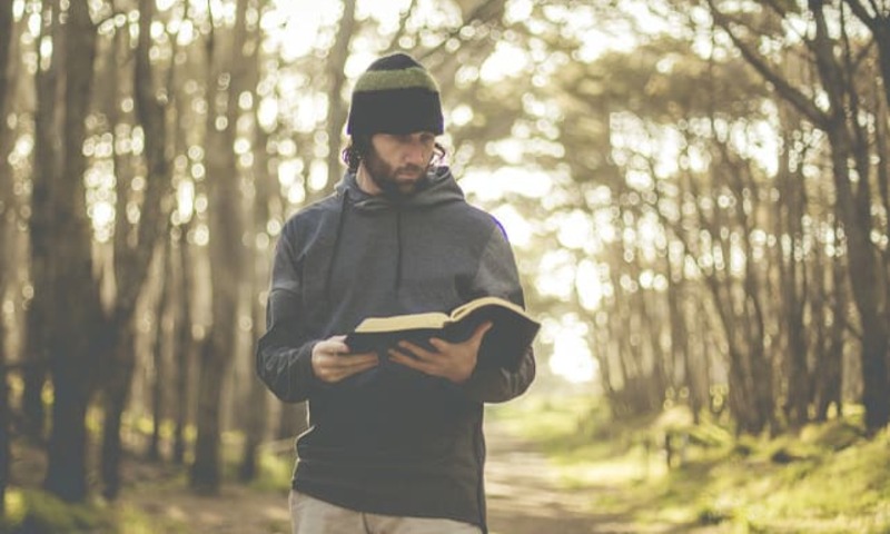 image shows a man holding a Bible in the woods