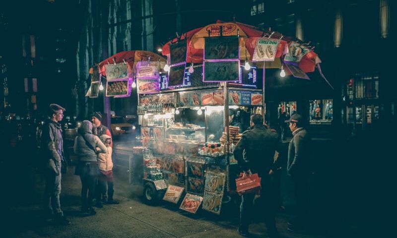Image shows street cart at night selling food to a waiting patrons