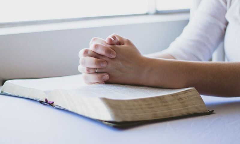 Image shows hands in prayer resting on Bible