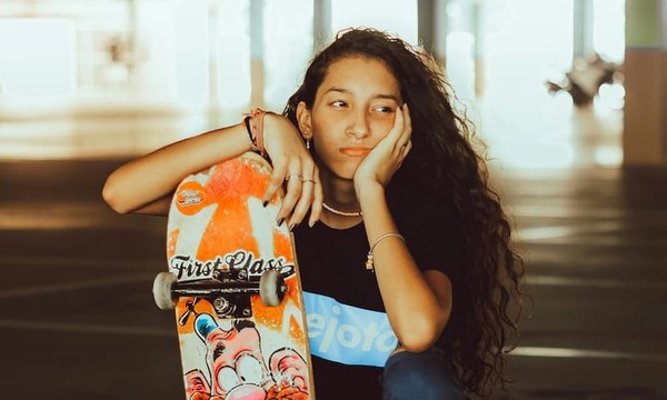 Woman in blue tank top holding orange and black skateboard