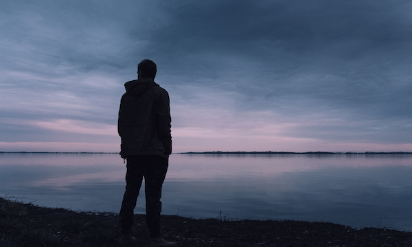 Person standing and watching purple sunset on a lake