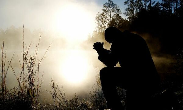Person in a prayer posture next to lake