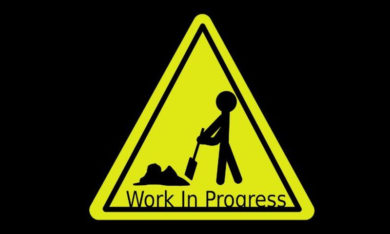 Image shows road sign with the words "Work in Progress" and man with shovel