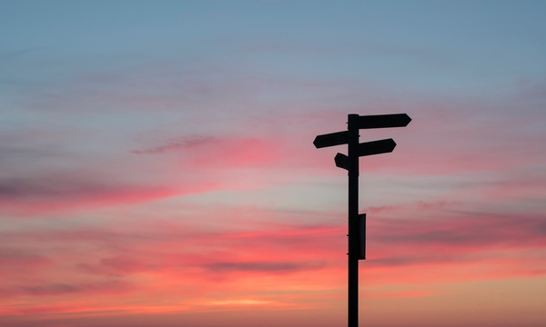 image shows directional signs against a sunset