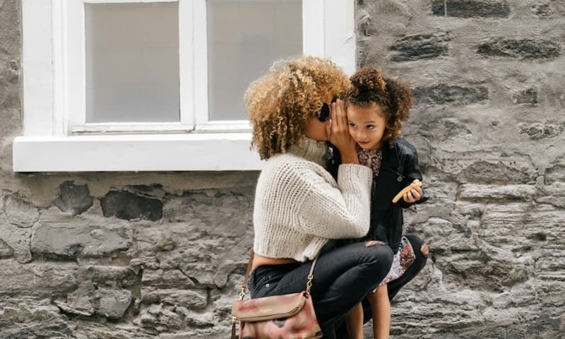 mother carrying her daughter whispering in her ear