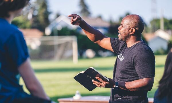 Coach on soccer field shares message with Bible in hand