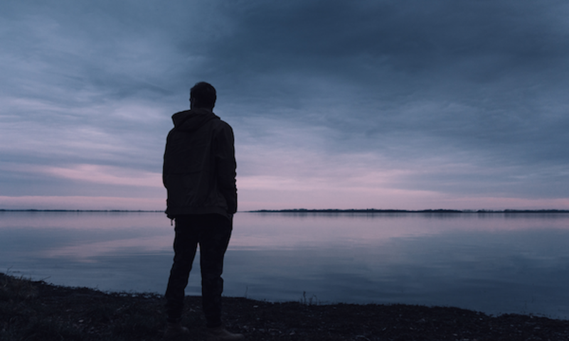 Person standing and watching purple sunset on a lake