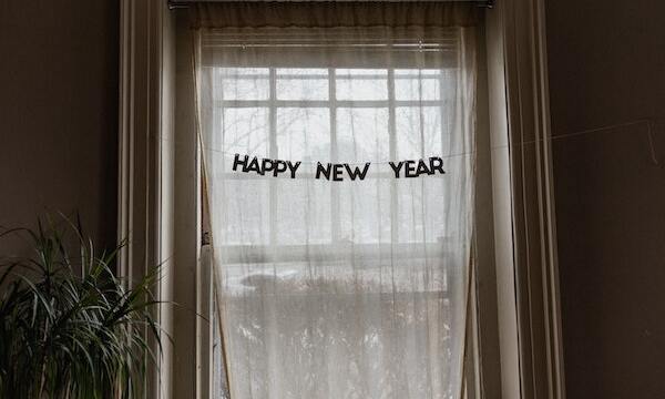 Image shows a "Happy New Year" sign hanging in a window. 