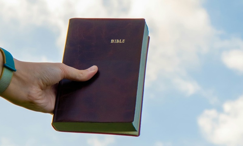 image shows a Bible in someone's hand against the sky