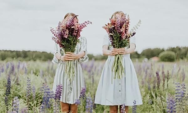 Two women standing with flowers in front of their faces.